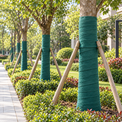 Green tree trunk wrap installed on landscaped trees along a garden walkway.